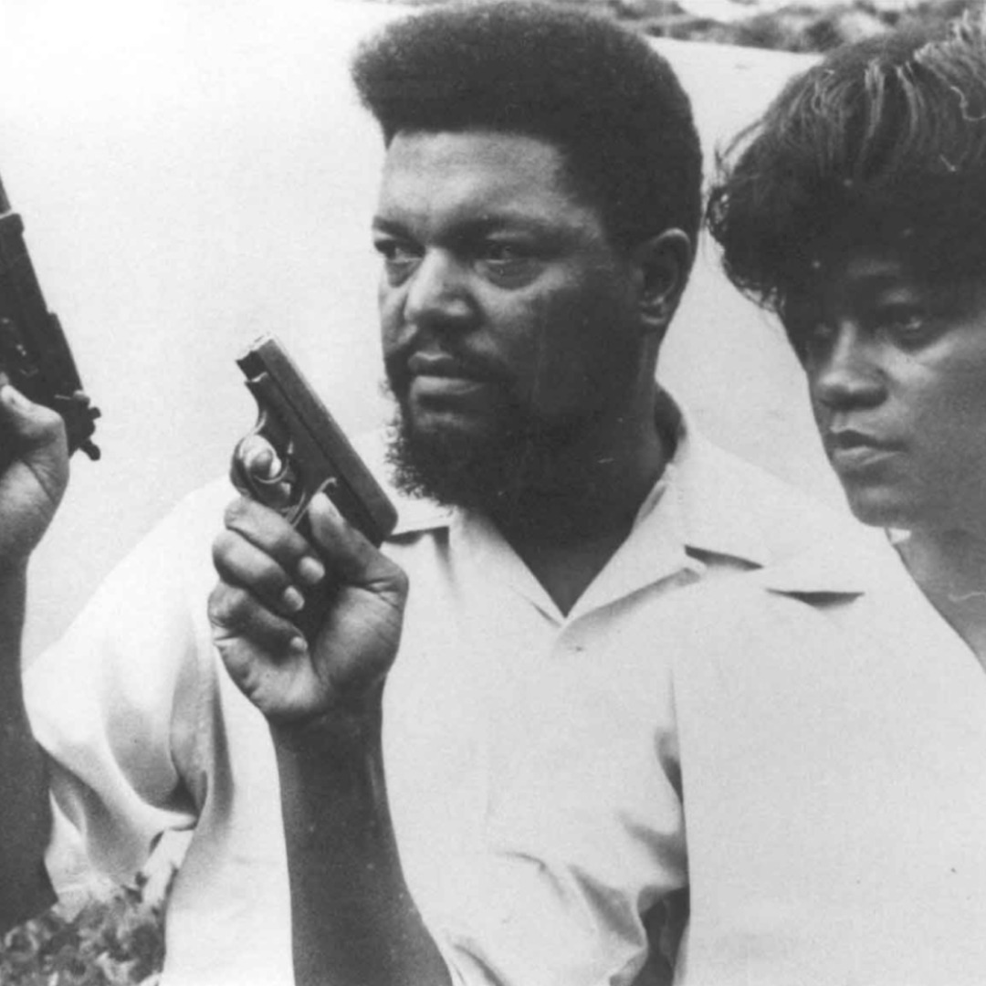 Photo en noir et blanc de Robert et Mabel williams de trois quarts, en gros plan buste, avec leur bras droit replié, armé chacun au bout d'un pistolet noir.
