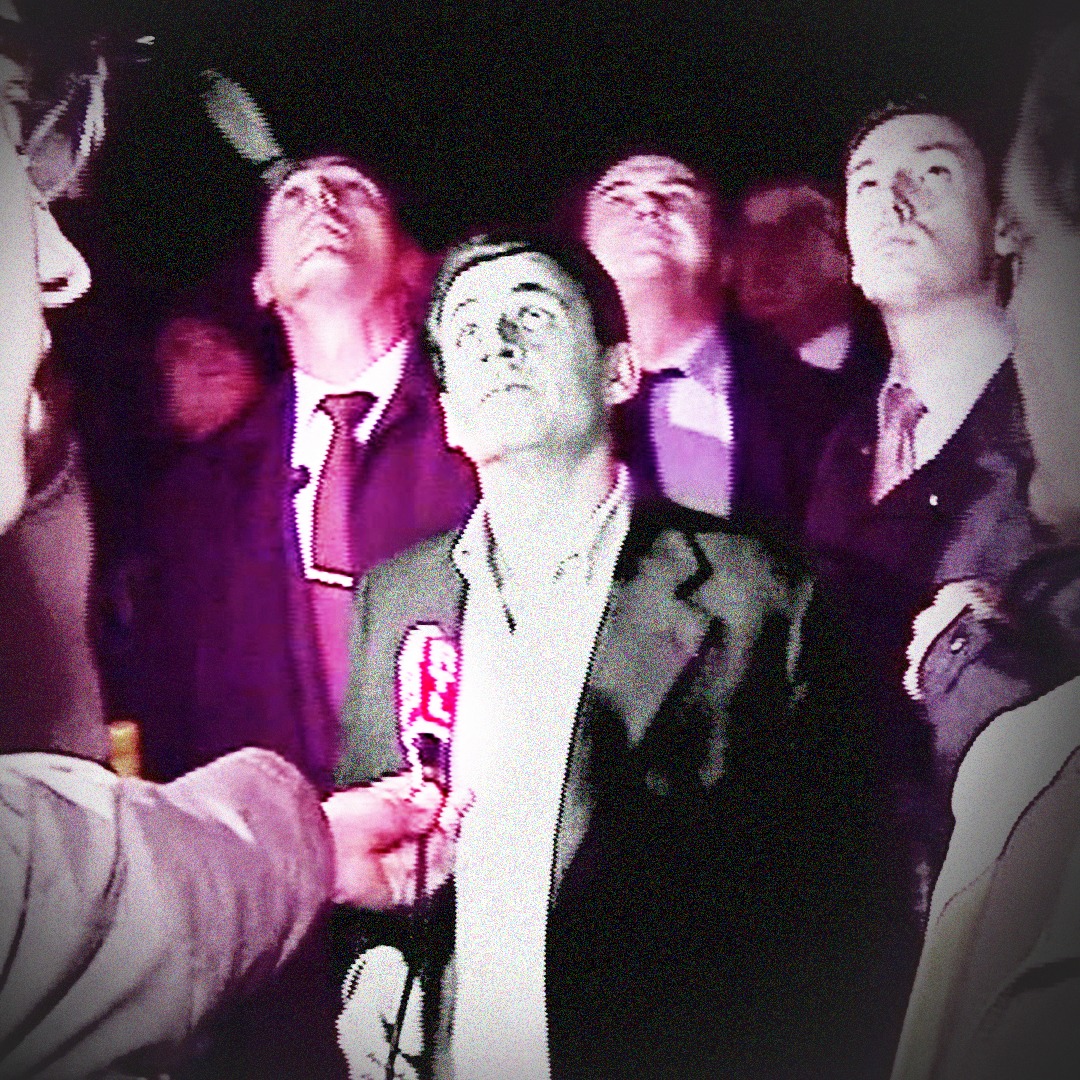 Image tiré d'un reportage montrant Nicolas Sarkozy, ministre de l'intérieur, le 25 octobre 2005, sur la dalle d’Argenteuil. Nicolas Sarkozy , en noir et blanc, est au milieu d'un groupe de 4 à 5 hommes. Tous regardent vers le haut. Du côté gauche de l'image de l'image, un journaliste dont on voit un quart de visage tend à Sarkozy un micro RTL. Du côté droit, un autre journaliste, visible au quart, regarde dans la direction de Sarkozy.