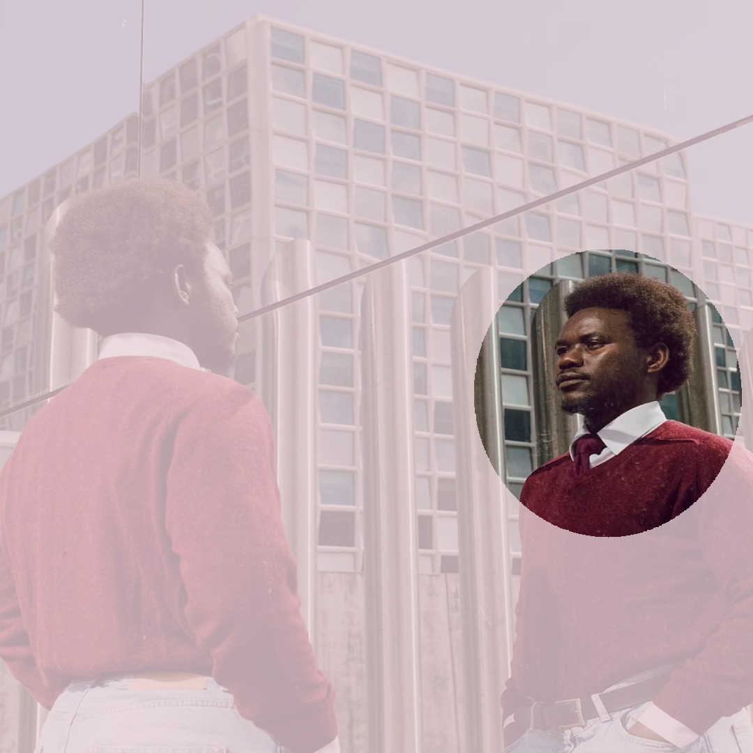 Photo en couleur de David Yambio un jeune homme noir, cadré à la taille, qui regarde son reflet dans un immeuble.